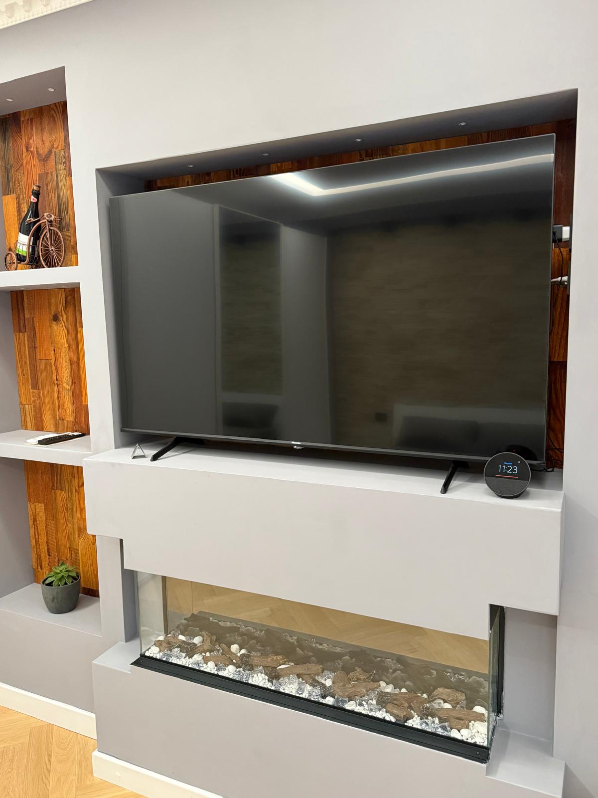 Tv e camino artificiale, piccole piante decorative e dettagli in legno.